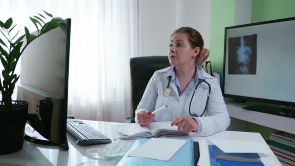 医療、女性医師は、オンラインの患者に相談してください医療室に座っているコンピュータとウェブカメラのビデオ接続を使用して病気の症状を伝える - 映像、動画