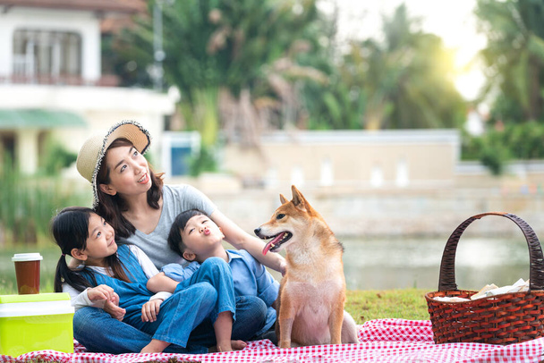 Haustierliebhaber. Eine asiatische Familie spielt mit einem Shiba-Inu-Hund. Familie hat Mutter und Sohn, Tochter. Picknick im Garten. - Foto, Bild