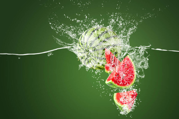 Water splashing on Slice of watermelon underwater on a green background. - Photo, Image