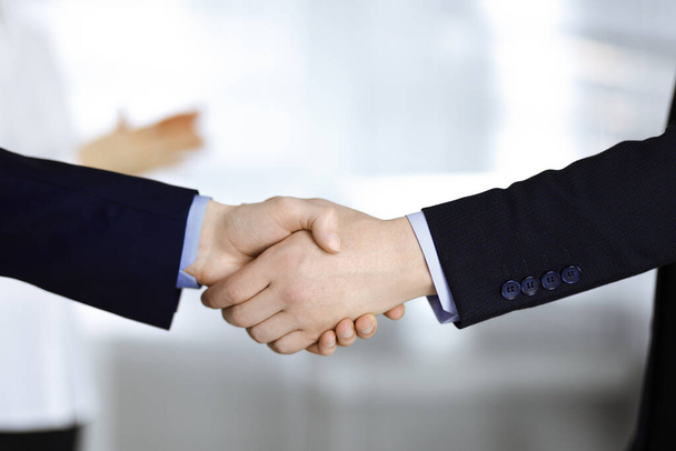 Business people shaking hands at meeting or negotiation, close-up. Group of unknown businessmen and a woman standing in a modern office. Teamwork, partnership and handshake concept - Foto, afbeelding