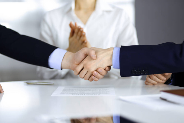 Business people shaking hands at meeting or negotiation, close-up. Group of unknown businessmen, and a woman on the background in a modern office. Teamwork, partnership and handshake concept - Foto, imagen