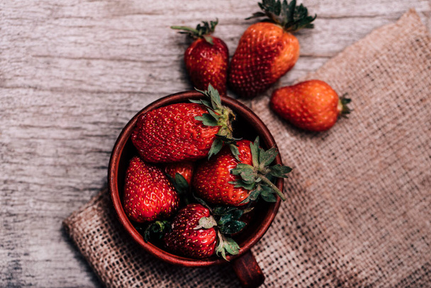 Small bowl filled with succulent juicy fresh ripe red strawberries on an old wooden textured table top. Fresh juicy organic strawberries in an old clay bowl. - Photo, Image