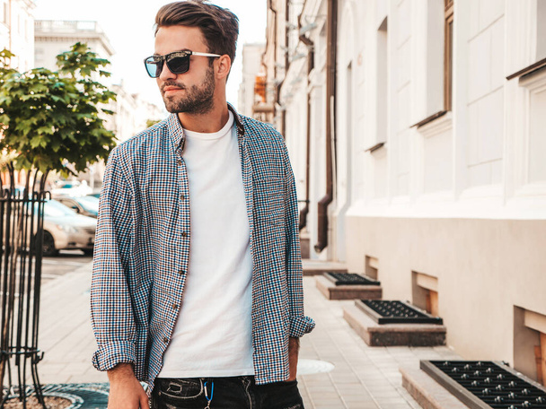Portrait of handsome confident stylish hipster lambersexual model.Man dressed in white T-shirt. Fashion male posing on the street background in sunglasses - Fotoğraf, Görsel