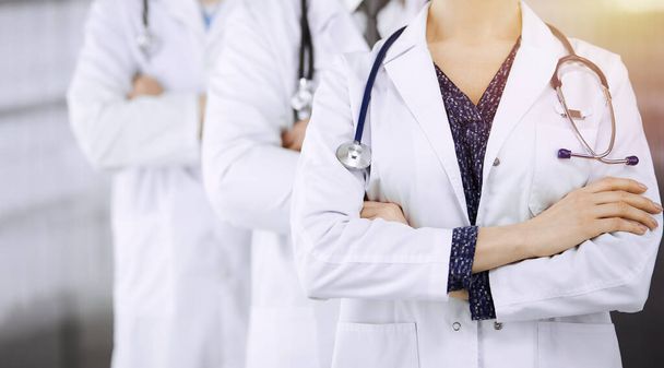 Doctors standing as a team with arms crossed in sunny clinic. Medical help, insurance and medicine concept - Photo, image