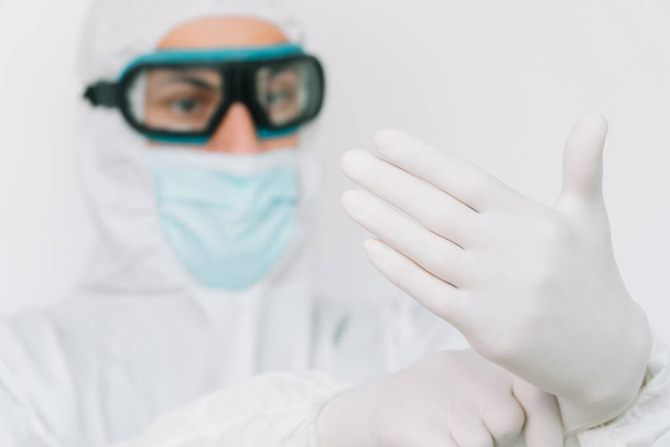 Virologist is weaing in protective clothe during virus pandemic, portrait. Suit, mask, gloves and glasses on white background in clinic or hospital - Foto, Bild