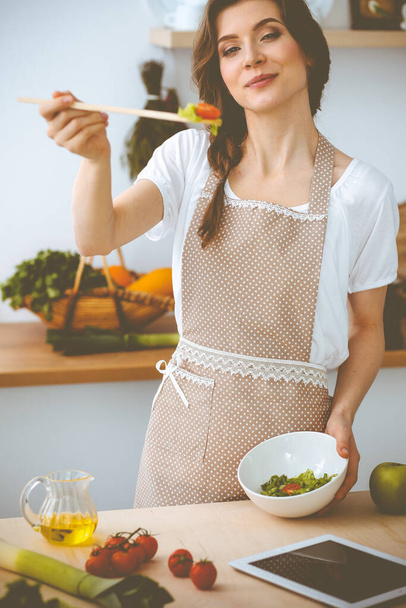 Young brunette woman cooking in kitchen. Housewife holding wooden spoon in her hand. Food and health concept - Photo, image