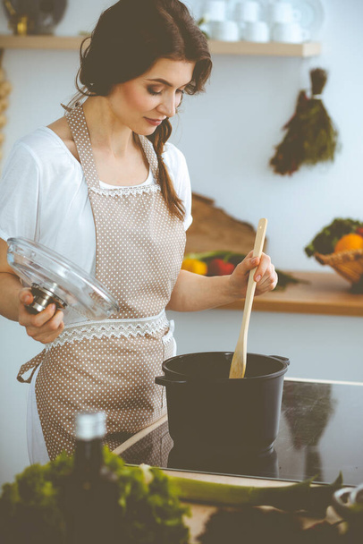 Young brunette woman cooking soup in kitchen. Housewife holding wooden spoon in her hand. Food and health concept - Fotoğraf, Görsel