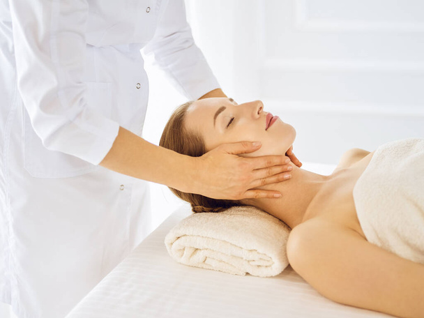 Beautiful woman enjoying facial massage with closed eyes - 写真・画像