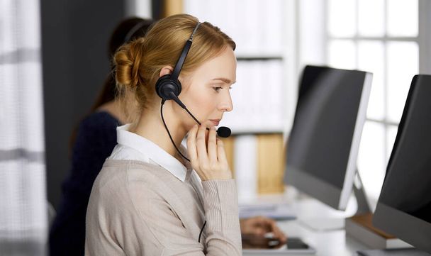 Friendly businesswoman talking by headset in office. Call center and diverse people group in business - Fotografie, Obrázek
