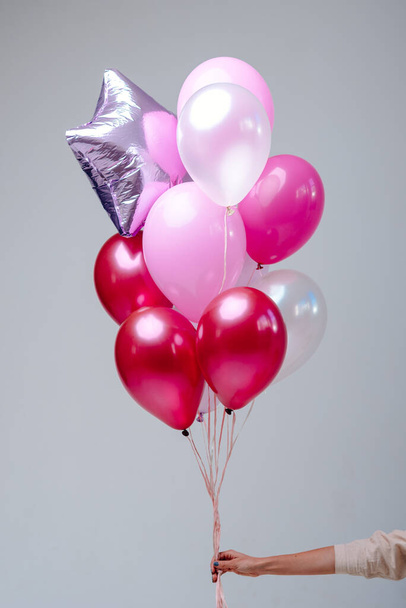Composition of red, pink, transparent helium balloons and silver star in the hand of a woman on a white background. - Fotoğraf, Görsel