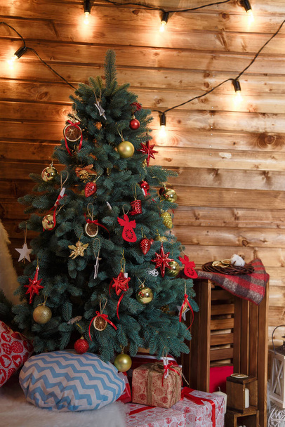 Feliz Navidad y Feliz Año Nuevo presenta de pie bajo el abeto decorado con bulbos rojos, juguetes y arcos. Concepto vacaciones de invierno
.  - Foto, imagen