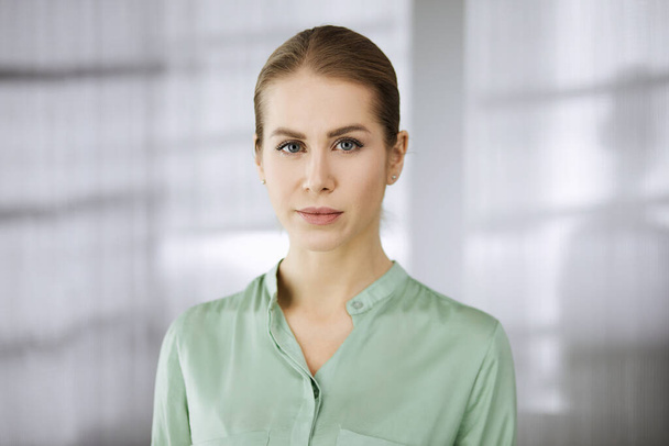 Beautiful adult business woman dressed in green blouse standing straight in office. Business headshot or portrait - Photo, Image
