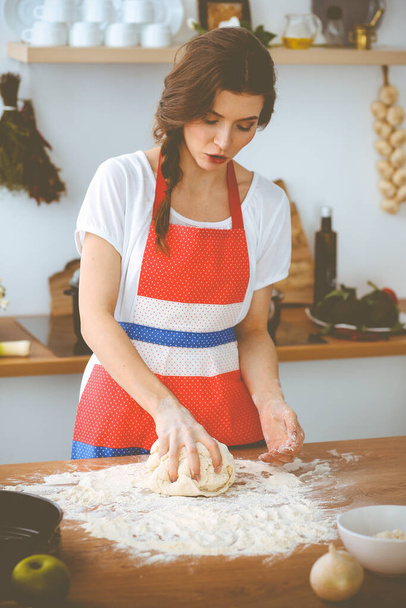 Young brunette woman cooking pizza or handmade pasta in the kitchen. Housewife preparing dough on wooden table. Dieting, food and health concept - Foto, immagini
