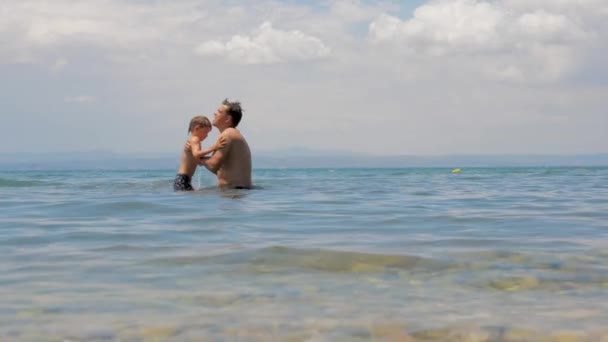 Happy European family playing at the sea. Dad and little son play and enjoy the sea water on the shore of lake, sea or ocean. Family vacation. Aegean sea, summer vacation. Winter holidays - 映像、動画