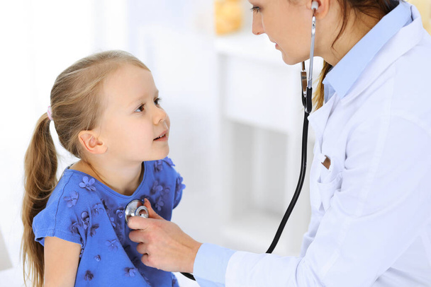 Doctor examining a little girl by stethoscope. Happy smiling child patient at usual medical inspection. Medicine and healthcare concepts - Foto, Imagen