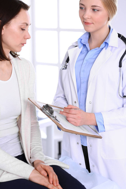 Young woman doctor and patient at medical examination at hospital office. Blue color blouse of therapist looks good. Medicine and healthcare concept - Photo, image