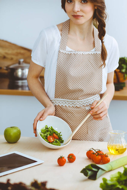 Mladá brunetka vaří v kuchyni. Hospodyně drží v ruce dřevěnou lžíci. Koncepce potravin a zdraví - Fotografie, Obrázek