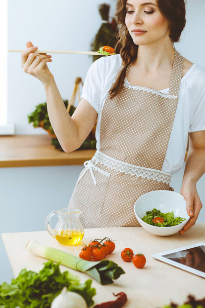 Young brunette woman cooking in kitchen. Housewife holding wooden spoon in her hand. Food and health concept - Фото, изображение