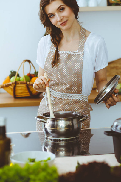 Young brunette woman cooking soup in kitchen. Housewife holding wooden spoon in her hand. Food and health concept - Foto, immagini