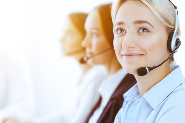 Group of diverse phone operators at work in sunny office. Handsome business woman with headphones consulting clients. Call center and business people concept - Fotografie, Obrázek