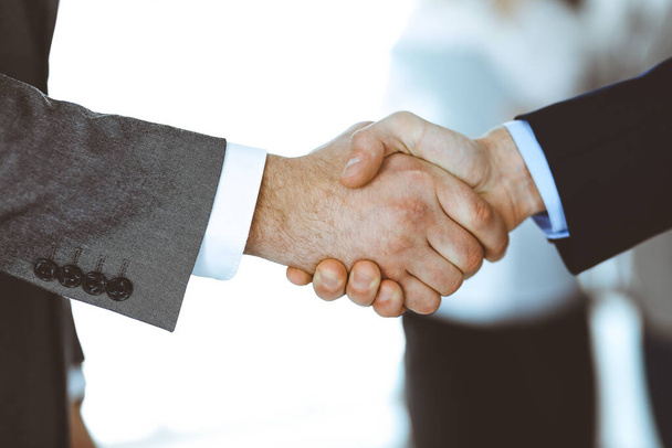 Business people shaking hands while standing with colleagues after meeting or negotiation, close-up. Group of unknown businessmen and women in modern office. Teamwork, partnership and handshake - Foto, Bild