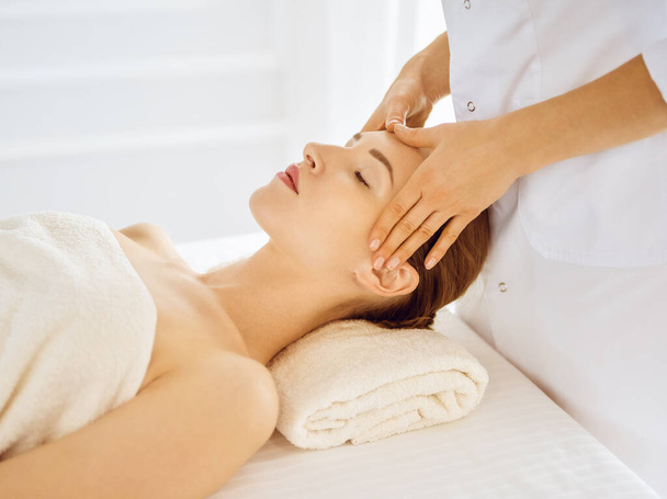 Beautiful woman enjoying facial massage with closed eyes in spa center. Relaxing treatment concept in medicine - Φωτογραφία, εικόνα