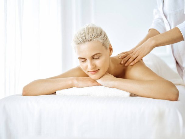 Beautiful blonde woman enjoying back massage with closed eyes. Spa salon concept - Foto, immagini