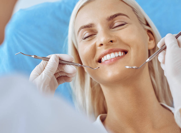 Smiling blonde woman examined by dentist at dental clinic. Healthy teeth and medicine concept - Foto, imagen
