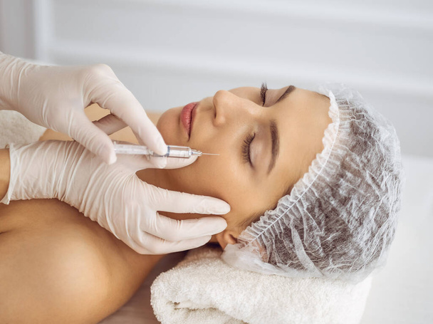 Beautician doing beauty procedure with syringe to face of young brunette woman. Cosmetic medicine and surgery, beauty injections - Foto, afbeelding