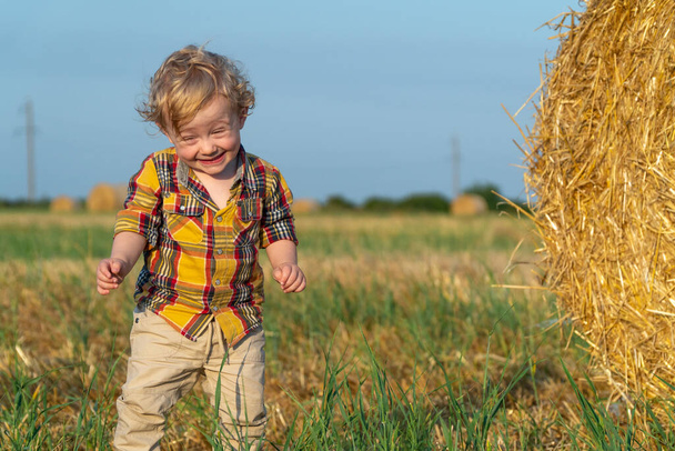 Маленький светловолосый мальчик играет на пшеничном поле с тюками - Фото, изображение