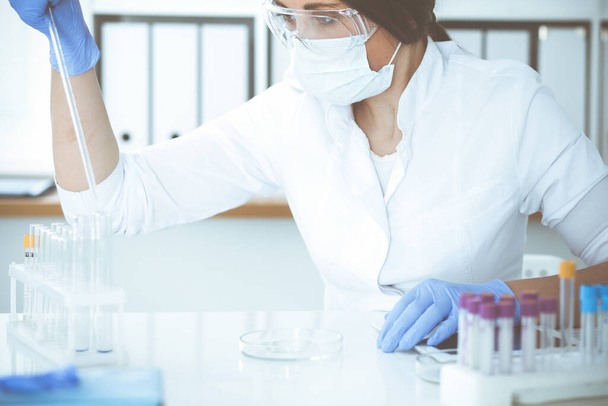Close-up of professional female scientist in protective eyeglasses making experiment with reagents in laboratory. Medicine and research concept - Foto, afbeelding