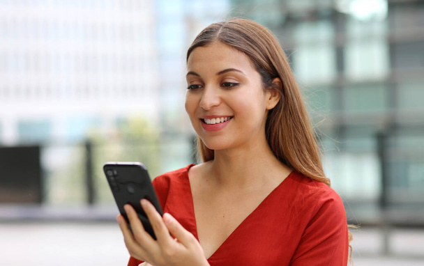 Portrét krásné příležitostné obchodní žena posílání zprávy s mobilní telefon chatování app s moderními mrakodrapy na pozadí - Fotografie, Obrázek