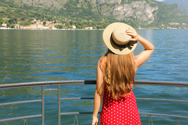 コモ湖の景色を楽しむ旅行者の女の子。イタリア、コモ湖のベッラージョのテラスでリラックスした若い女性のリアビュー. - 写真・画像