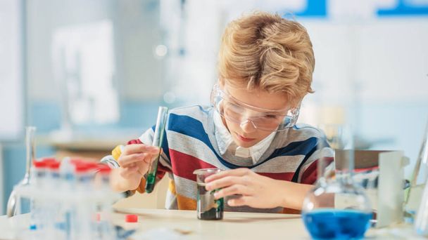 Elementary School Science or Chemistry Classroom: Smart Little Boy wearing Safety Glasses Mixes Chemicals in Beakers - Zdjęcie, obraz