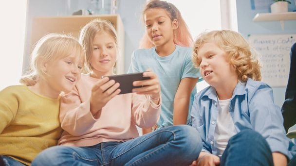Diverse Group of Cute Small Children Sitting together on the Bean Bags Use Smartphone and Talk, Have Fun. Kids Browsing on Internet and Playing Online Video Games on Mobile Phone, Watching Videos - Foto, Imagem