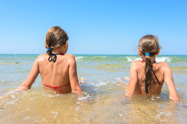Дети сидят в воде на побережье и смотрят вдаль
 - Фото, изображение