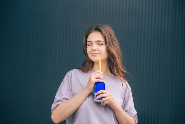 Νεαρή κομψή μοντέρνα γυναίκα απομονωμένη πάνω από γκρι μπλε φόντο. Κορίτσι απολαμβάνει το χρόνο της μόνη στο σκοτεινό τοίχο πίνοντας σόδα. Κομψή γυναίκα σε βιολετί πουκάμισο. - Φωτογραφία, εικόνα