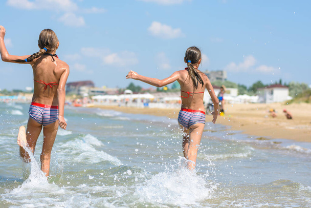 Dwie dziewczyny radośnie biegają wzdłuż morza w ciepły letni dzień, widok z tyłu - Zdjęcie, obraz