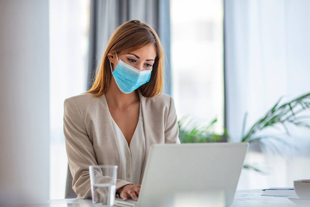 Female employee wearing medical face mask while working in the business office during covid-19 pandemic. Businesswoman wearing face mask while analzying reports in the office.  - Фото, изображение