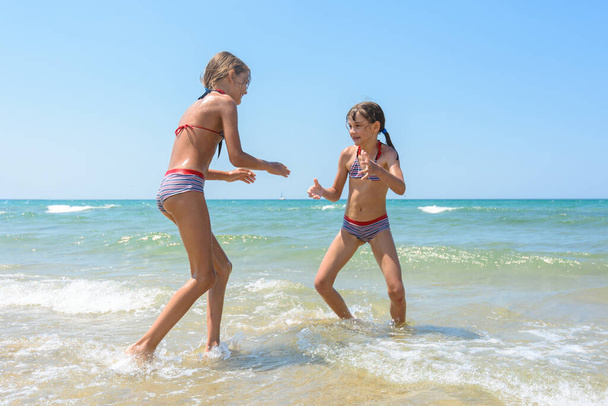 Δύο κορίτσια που παίζουν ξύλο στην παραλία μέσα στο νερό. - Φωτογραφία, εικόνα