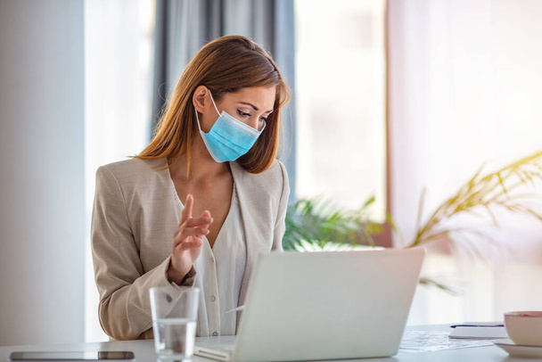 Businesswoman with protective face mask at office. Woman in the office working while wearing medical face mask during COVID-19. Woman wearing protective face mask for safety and protection during COVID-19 - Фото, изображение