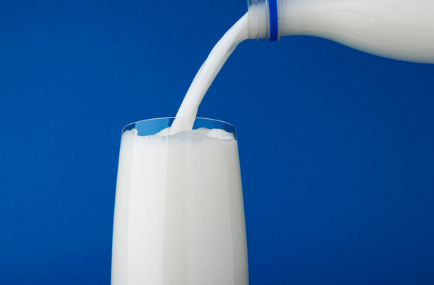 Giet melk in glas met splash geïsoleerd op blauwe achtergrond - Foto, afbeelding