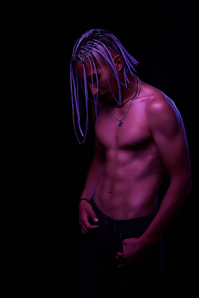 πορτρέτο ενός νέου γυμνού Αφρικανού στο στούντιο. Υψηλής μόδας ανδρικό μοντέλο σε πολύχρωμο νέον φωτεινά φώτα που θέτουν σε μαύρο φόντο. Σχέδιο τέχνης. επιλεκτική εστίαση. - Φωτογραφία, εικόνα