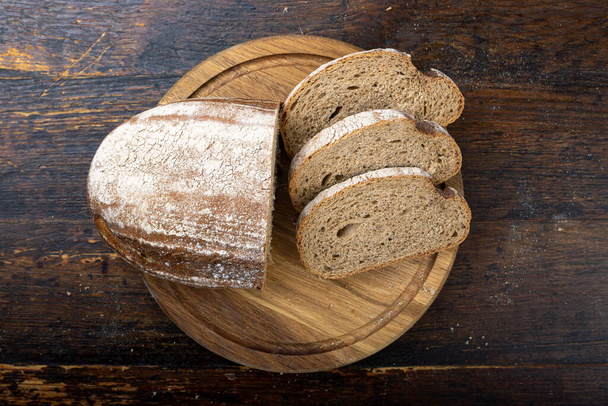 Świeży chleb pieczony i chleb krojony na wiejskim drewnianym stole. - Zdjęcie, obraz