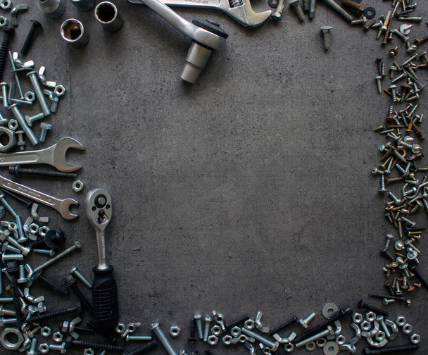 Old bolts and nuts on dark grey concrete background. Frame or border. Textured background with copy space. - 写真・画像