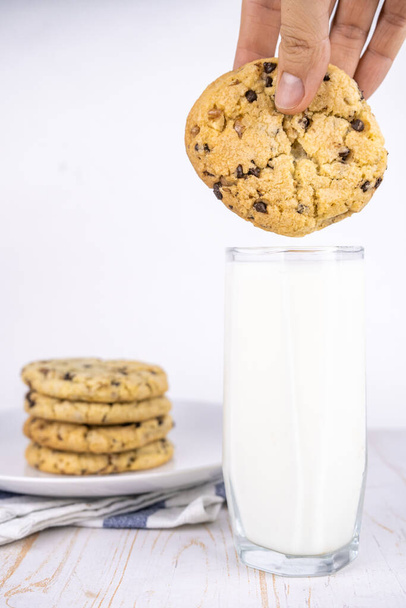 φρεσκοψημένα κλασικά μπισκότα σοκολάτας με ξηρούς καρπούς σε ένα πιάτο και ένα ποτήρι γάλα - Φωτογραφία, εικόνα