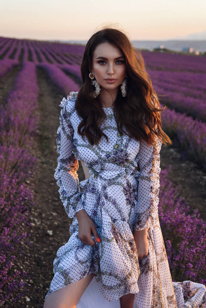 fashion outdoor photo of beautiful sensual woman with dark hair in elegant dress with accessories posing in blooming lavender field - Fotografie, Obrázek