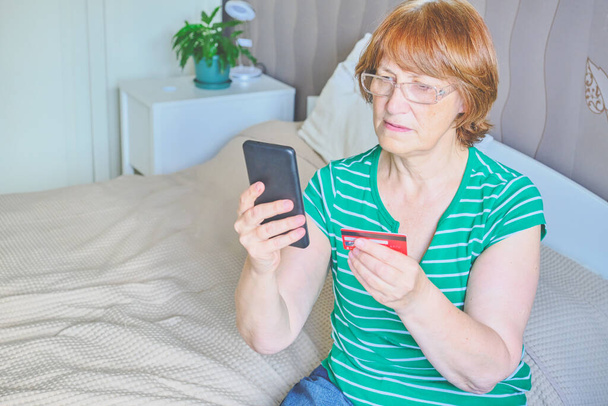 Donna anziana che usa un telefono in camera da letto a casa. Buon pensionato shopping online sul letto. Stile di vita. Copia spazio - Foto, immagini