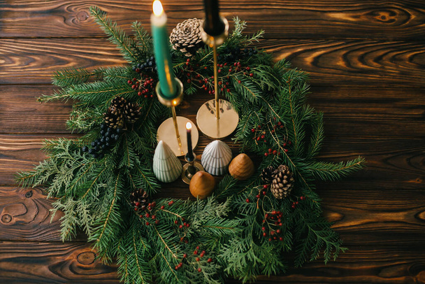 Mutlu noeller. Yılbaşı ağaçları ve mumlar koyu renkli ağaçların üzerinde Noel çelengi. Şenlikli modern dekor. Minyatür çam ağaçları, şamdan ve böğürtlen ve kozalaklı modern çelenk. - Fotoğraf, Görsel