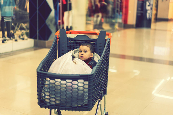 Egy kocsi olyan termékekkel, amelyeken a gyermek ül. Tele bevásárlókocsi étellel a szupermarketben. A kocsiban ül egy kisbaba. tónusú. - Fotó, kép